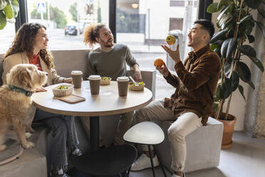 Businessman juggling fruits sitting with colleagues at office cafe - JCCMF11314