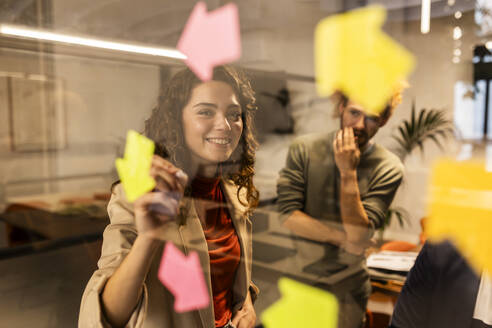 Smiling businesswoman behind glass with colleague at office - JCCMF11327