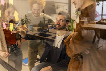 Geschäftsmann beim Brainstorming mit Kollegen hinter einer Glaswand im Büro - JCCMF11332