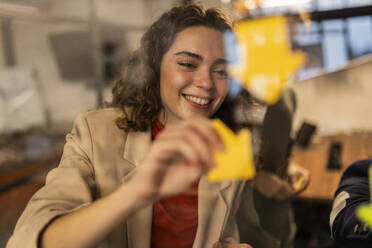 Smiling businesswoman sticking adhesive notes on glass wall at home - JCCMF11333