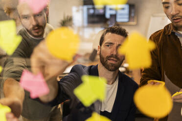 Businessman discussing with colleagues in meeting behind glass wall - JCCMF11335