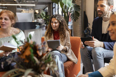 Smiling businesswoman holding tablet PC sitting with colleagues at office - JCCMF11347