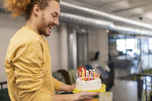 Happy businessman holding illuminated birthday cake at office - JCCMF11355