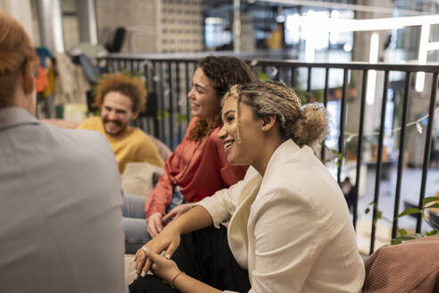 Lächelnde Geschäftsfrau, die im Co-Working Space mit Kollegen sitzt und spricht - JCCMF11358