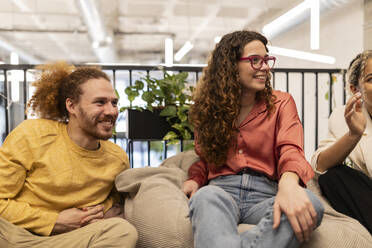 Geschäftsfrau mit lockigem Haar sitzt inmitten von Kollegen im Co-Working Space - JCCMF11360