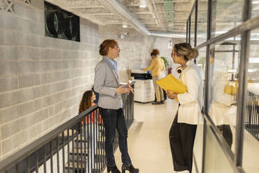 Businesswomen discussing with each other at office corridor - JCCMF11366