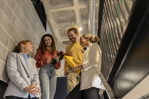 Happy business colleagues discussing on staircase at office - JCCMF11371