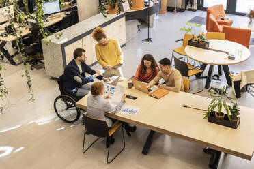 Businessman working with colleagues sitting at desk in office - JCCMF11373