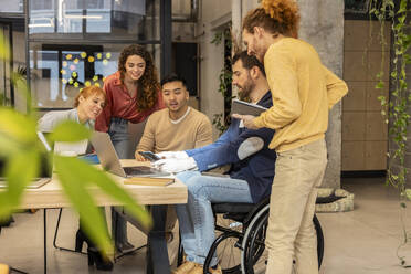 Businessman sitting in wheelchair and discussing with colleagues at office - JCCMF11377