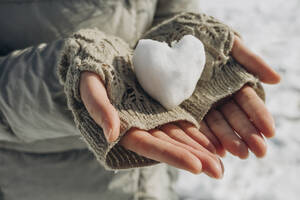 Woman holding heart shaped snowball in hand - KVBF00002
