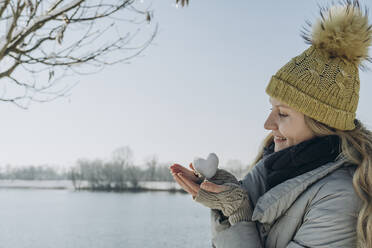 Glückliche Frau mit herzförmigem Schneeball am See - KVBF00006