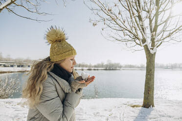 Woman with heart shaped snowball in hand near lake - KVBF00007