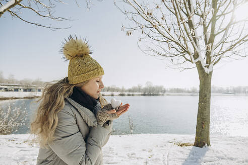 Frau mit herzförmigem Schneeball in der Hand am See - KVBF00007