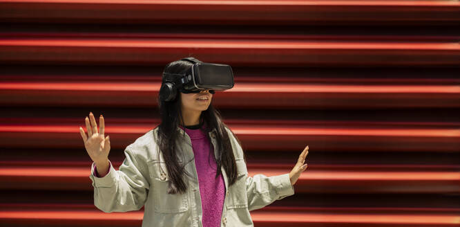 Happy young woman gesturing with virtual reality simulators - JCCMF11412
