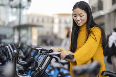 Glückliche junge Frau, die ein Elektrofahrrad in der Stadt mietet - JCCMF11430