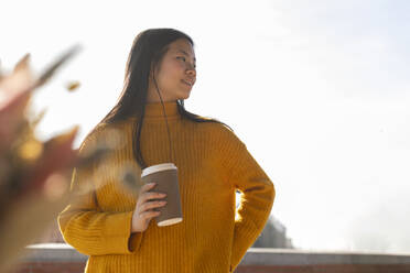 Happy woman holding disposable coffee cup under sky - JCCMF11443