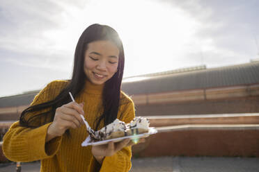 Lächelnde junge Frau isst Waffel an einem sonnigen Tag - JCCMF11447