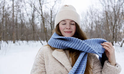 Junge lächelnde Frau mit geschlossenen Augen und blauem Schal im Winterwald - MBLF00273