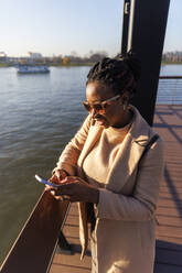 Lächelnde Frau mit Smartphone in der Nähe des Flusses - IKF01723