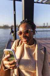 Glückliche Frau mit Videoanruf auf Smartphone in der Nähe des Flusses - IKF01725