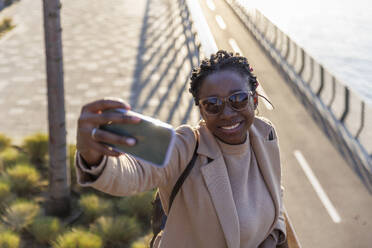 Smiling woman taking selfie through mobile phone - IKF01728