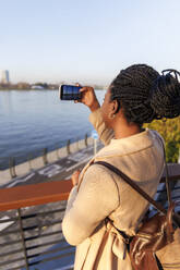 Frau fotografiert Fluss bei Sonnenuntergang mit dem Mobiltelefon - IKF01737