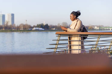 Smiling woman using smart phone near railings - IKF01738