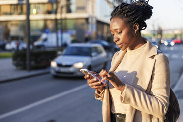 Woman using smart phone on street at sunset - IKF01742