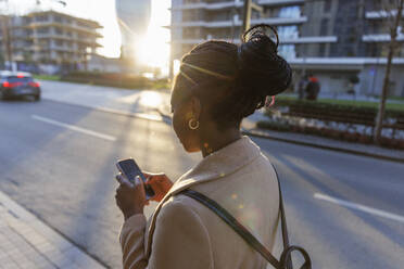 Woman using smart phone in city at sunset - IKF01745