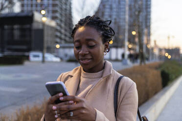 Woman using smart phone on street in city - IKF01756