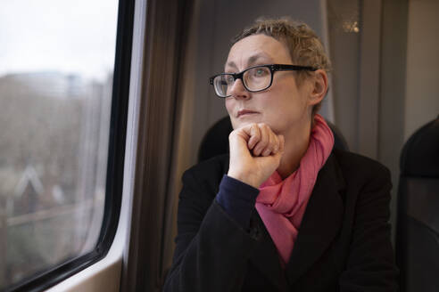 Thoughtful businesswoman wearing eyeglasses and traveling in train - AMWF02025