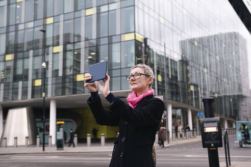 Geschäftsfrau, die mit einem Tablet-PC vor einem Gebäude fotografiert - AMWF02029