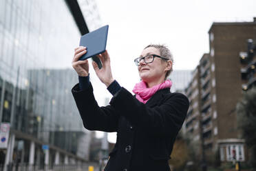 Mature businesswoman taking picture through tablet PC in city - AMWF02030