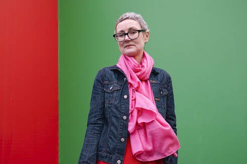 Mature woman wearing eyeglasses standing in front of green wall - AMWF02035