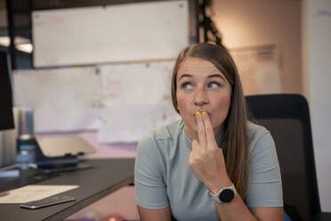 Junge Geschäftsfrau sitzt mit Fingern auf den Lippen im Büro - JOSEF23485