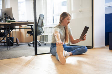 Geschäftsfrau hält Tablet-PC und streckt Bein im Büro - JOSEF23496