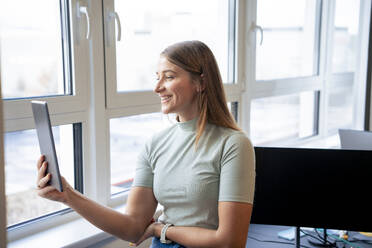 Smiling businesswoman having video call on tablet PC in office - JOSEF23499