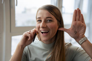 Cheerful businesswoman showing heart drawn on palm in office - JOSEF23500