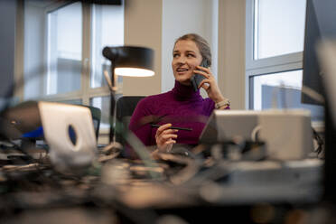Geschäftsfrau hält Stift und spricht auf Smartphone im Büro - JOSEF23520