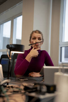 Playful businesswoman balancing pen between nose and lips in office - JOSEF23524