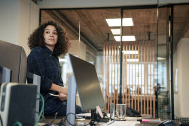 Nachdenkliche Geschäftsfrau sitzt auf dem Schreibtisch neben dem Computer im Büro - JOSEF23533