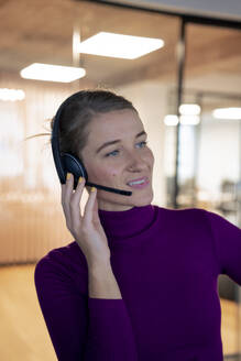 Lächelnder Kundendienstmitarbeiter im Gespräch mit einem Kunden über ein Headset im Büro - JOSEF23541