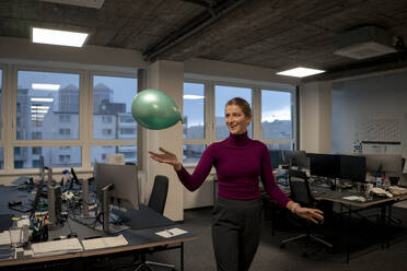 Happy young businesswoman playing with balloon in office - JOSEF23552