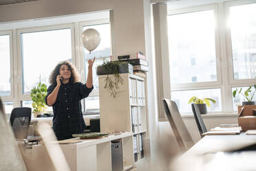 Businesswoman playing with balloon in office - JOSEF23553