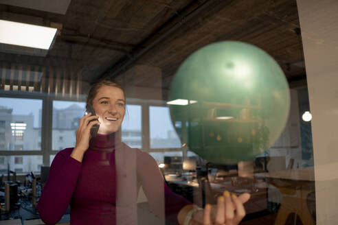 Glückliche Geschäftsfrau im Gespräch auf dem Smartphone und spielen mit Ballon im Büro - JOSEF23555