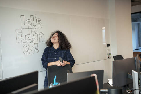 Happy businesswoman standing near whiteboard in office - JOSEF23559