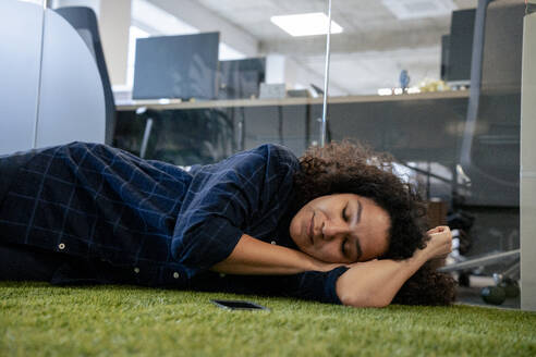 Geschäftsfrau beim Nickerchen auf grünem Teppich im Büro - JOSEF23578