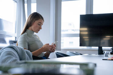 Geschäftsfrau, die im Büro sitzt und ein Smartphone benutzt - JOSEF23583