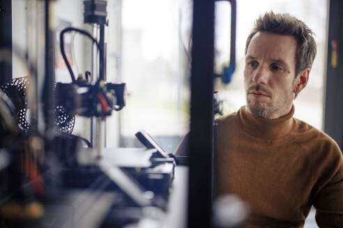 Engineer looking at machinery in glass box at workshop - JOSEF23597