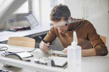 Focused engineer repairing machine part through soldering iron at workshop - JOSEF23618